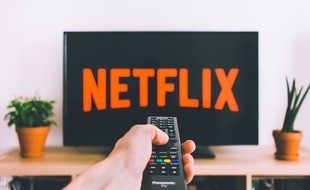 Personne tenant une télécommande avec le bouton « Netflix » allumant l'application sur l'écran d'une télévision.