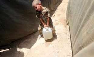 Un petit irakien dont la famille a fui Ramadi, porte un jerrican d'eau dans un camps de réfugiés, le 18 mai 2015 à Bzeibez à la frontière de Bagdad et Anbar