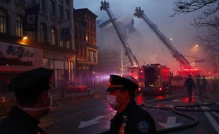 Des policiers new-yorkais devant les lieux d'un incendie avec en arrière plan les pompiers qui luttent pour circonscrire un incendie à New York le 26 mars 2015