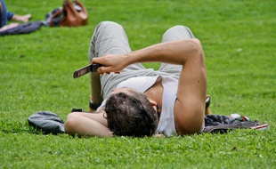 Homme allongé dans un parc lisant ses textos sur son téléphone mobile.