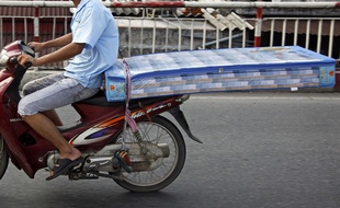 Un homme transportant un matelas sur un scooter (illustration).