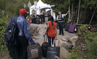 Un officier de la police canadienne fait face à un couple de migrants en provenance des Etats-Unis. Un point de passage temporaire a dû être aménagé près de Saint-Bernard-de-Lacolle (Québec).