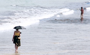 Une femme marche avec une ombrelle pour se protéger du soleil sur la plage de Dinard (Ille-et-Vilaine)