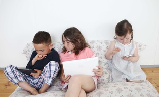 Trois enfants utilisent différents appareils électroniques dans le salon;