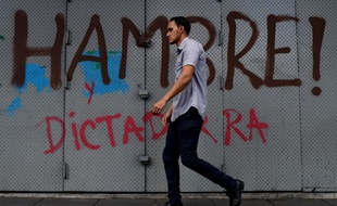 Un homme marche devant les mots faim et dictature écrits sur un mur de Caracas.