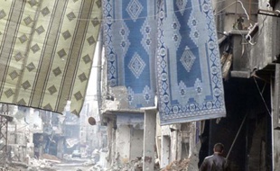 Un milicien du régime marche sous des tapis servant à contrer les snipers dans une rue dévastée de la banlieue de Damas, en Syrie.