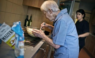 Une personne âgée prépare un gâteau sous l'oeil attentif d'une aide de vie, en Bourgogne en juillet 2011