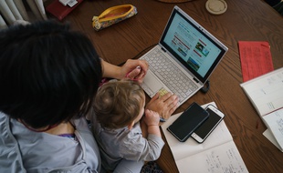 Une femme télétravaille en gardant son enfant.