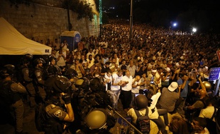 Des forces de sécurité israéliennes se tiennent devant des fidèles musulmans palestiniens qui prient le 23 juillet 2017 à l'extérieur de la porte des Lions, entrée principale de la mosquée Al-Aqsa à Jérusalem, afin de protester face aux nouvelles mesures de sécurité imposées par Israël.