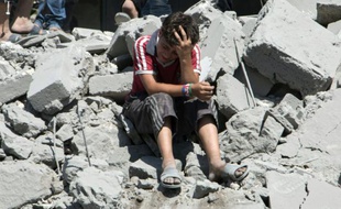 Un jeune garçon est effondré le 21 juillet 2015 sur les décombres de maisons dans un vieux quartier d'Alep, au nord de la Syrie, bombardé par l'aviation syrienne