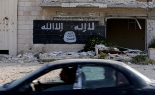 Des Syriens passent en voiture devant une usine détruite où a été peint le drapeau de Daesh, à Alep, le 18 novembre 2014.