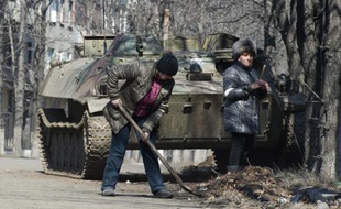 Des habitants de la ville de Debaltseve, dans l'est de l'Ukraine, nettoient leurs rues devant un char immobilisé, le 9 mars 2015