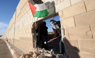 De jeunes Palestiniens brandissent un drapeau palestinien à travers la brèche qu'ils ont creusée dans le mur de séparation entre Israël et le village de Bir Nabala, en Cisjordanie, le 8 novembre 2014