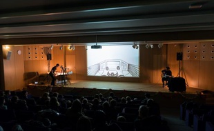 Jean-Charles Andrieu en plein dessin à gauche de la scène, Matthieu Chiara guitare à la main, à droite, avec l'écran de vidéoprojection au centre.