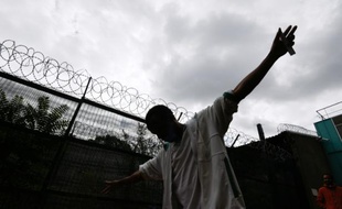Un migrant lève les mains au ciel près des barbelés qui entourent le centre d'hébergement Emmaüs où il réside, le 4 août 2015 à Vincennes