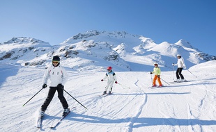 ather skiing in front of his children and wife on flat slope in the mountains