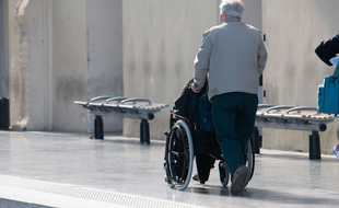 Un voyageur handicapé et son accompagnant sur un quai de gare. (Illustration)