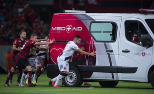 Les Brésiliens Everton Ribeiro (à gauche), Piris da Motta (à droite) et le Brésilien Vasco da Gama, Andrey (R), et d'autres coéquipiers des deux équipes poussent l'ambulance transportant le joueur blessé de Vasco da Gama, Bruno Silva.
