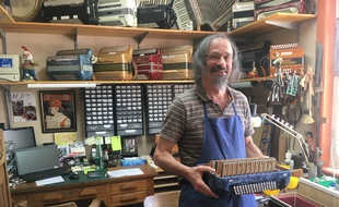 François Legris dans son atelier, portant un des accordéons qu'il est en train de réparer.
