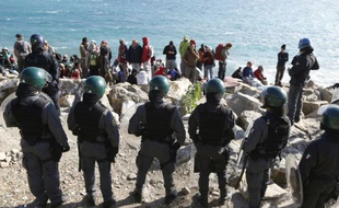 Des migrants attendent sur les rochers en bord de mer sous la surveillance de policiers, sur la frontière franco-italienne, à Vintimille, le 30 septembre 2015