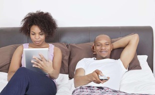 Un couple au lit avec une tablette et une télévision.