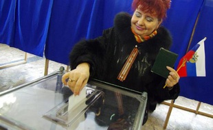 Une femme dépose son bulletin dans l'urne, drapeau russe à la main, le 16 mars 2014 à Sébastopol