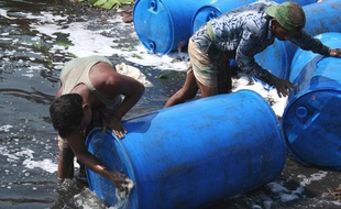 Des hommes nettoient des containers remplis de substances toxiques dans une rivière du Bangladesh, à Dhaka en mai 2007.