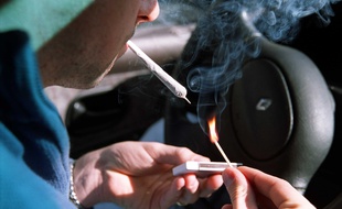 Un homme allume un joint de cannabis au volant de sa voiture. Illustration.