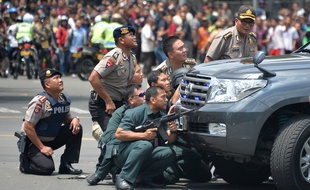 Des policiers indonésiens s'abritent derrière un véhicule alors que des explosions ont retenti à Djakarta, le 14 janvier 2016.