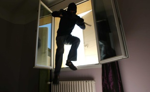 Illustration d'un cambrioleur qui s'introduit dans un appartement par une fenêtre ouverte.