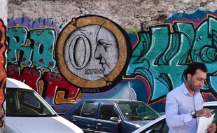 Un homme marche le 25 mai 2015 devant un graffiti montrant une pièce de "0 euro" dessiné sur le mur d'un parking d'Athènes.