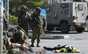 Des soldats israéliens portent secours à un des leurs (g) alors que le corps du palestinien auteur du coup de couteau gît au sol (d) à l'entrée d'Hébron en Cisjordanie occupée, le 16 octobre 2015