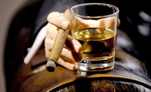 Un homme boit du whisky en fumant un cigare.