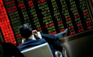 Un investisseur lit un journal devant un écran de cotation à Pékin le 20 janvier 2016
