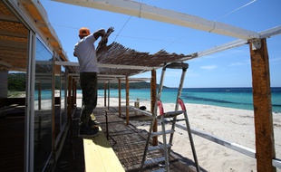 Un homme construit une paillotte sur la plage de Chivarari en Corse.