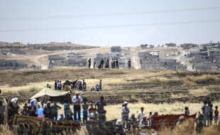 Des soldats turcs (au 1er plan) montent la garde alors que des Kurdes syriens se massent derrière des barbelés du côté syrien de la frontière turco-syrienne, près de Kobané, le 26 juin 2015.