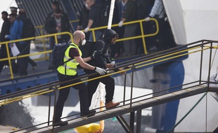 Un agent de Frontex escorte un migrant embarquant à bord d'un bateau à Lesbos, en Grèce, à destination de la Turqiue.