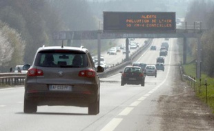 Des voitures passent sous un panneau d'avertissement du pic de pollution.