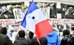 Un homme tient un drapeau français percé d'une fleur noire pendant la minute de silence en hommage aux victimes des attentats, place de la République le 16 novembre 2015