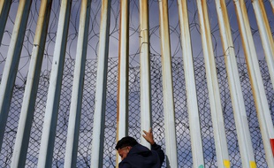 Un homme s'accroche au mur qui le sépare des Etats-Unis, le long de la plage de Tijuana, au Mexique.