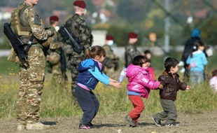 Des enfants jouent près de soldats slovènes, devant la file de migrants et réfugiés venant de passer la frontière, le 26 octobre 2015