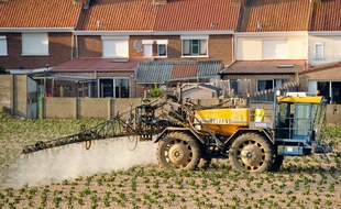 Un agriculteur traite un champ à proximité d'habitations.