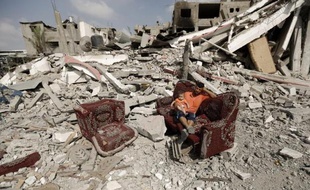 Un Palestinien assis sur un sofa avec un enfant au milieu d'un champs de ruines à Al-Shejaea (banlieue de Gaza City), le 5 août 2014