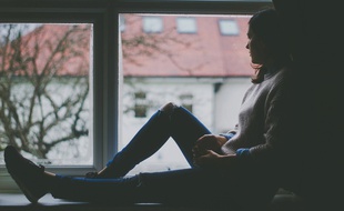 Une femme chez elle regarde par la fenêtre.