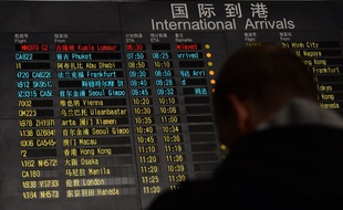 Un homme se tient devant le panneau d'affichage des arrivées à Pékin le 8 mars 2014. Le vol Kuala Lumpur-Pékin est affiché "en retard".