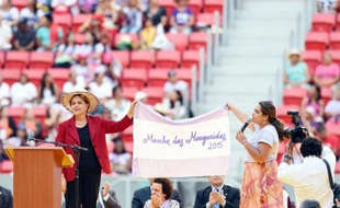 La présidente brésilienne Dilma Rousseff (g) et une dirigeante de la Confédération des travailleurs agricoles déploient un drapeau lors de la clôture de la marche des femmes des zones rurales, le 12 août 2015 à Brasilia