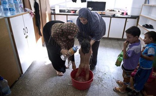 Feriel al-Zaaneen lave sa fille Sama dans une bassine à l'aide de bouteilles d'eau dans une école de l'ONU à Jabalia le 16 août 2014