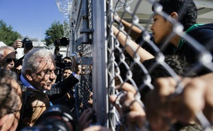 Le commissaire européen aux Migrations, Dimitris Avramopoulos (G) s'adresse à des enfants à travers la grille du camp de migrants de Moria, près de Mytilène, sur l'île grecque de Lesbos, le 16 octobre 2015