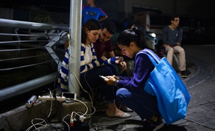 Des Vénézuéliens rechargent leur téléphone dans des magasins où il reste du courant alors qu'une nouvelle panne d'électricité plonge dans la pénurie et le noir le pays, déjà affecté par une immense panne du 7 au 14 mars 2019.