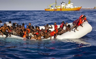 Des migrants en détresse attendent d'être secourus par l'Aquarius, le bâteau d'SOS Méditerranée (au fond).
